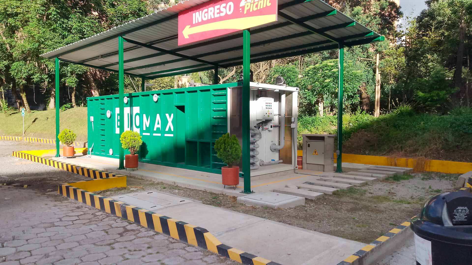 Técnico inspeccionando una planta de tratamiento de aguas residuales modular de color verde marca BIOMAX SYNERTECH, que incluye módulos de pretratamiento, decantación, DAF y oxidación avanzada. La planta está ubicada en un entorno industrial con techo alto y tuberías visibles. - ver más información